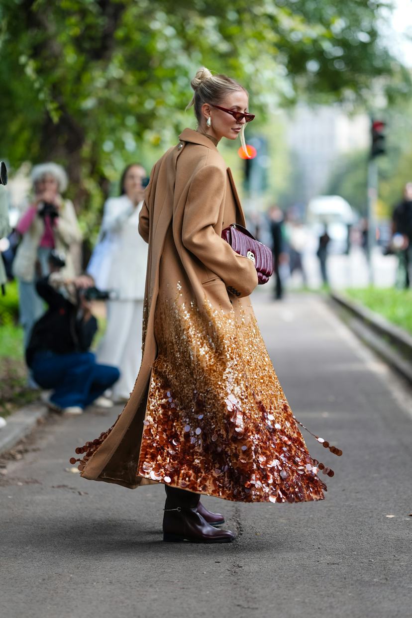 Ospite della Settimana della Moda che indossa un cappotto color cammello con paillettes e una borsa bordeaux per le vie della città.